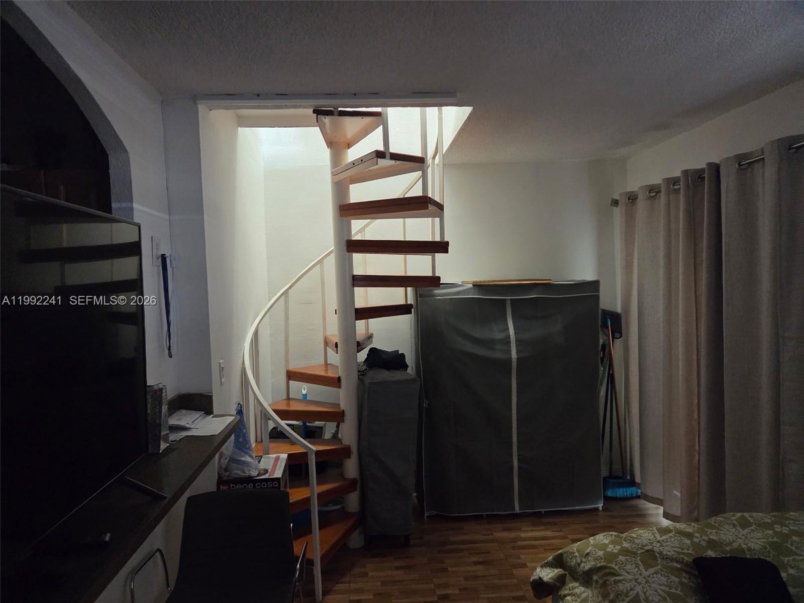 A spiral staircase stands in a room with a portable closet and a television — 6580 W Flagler St # 101, Miami FL 33144, MIAMI, FL