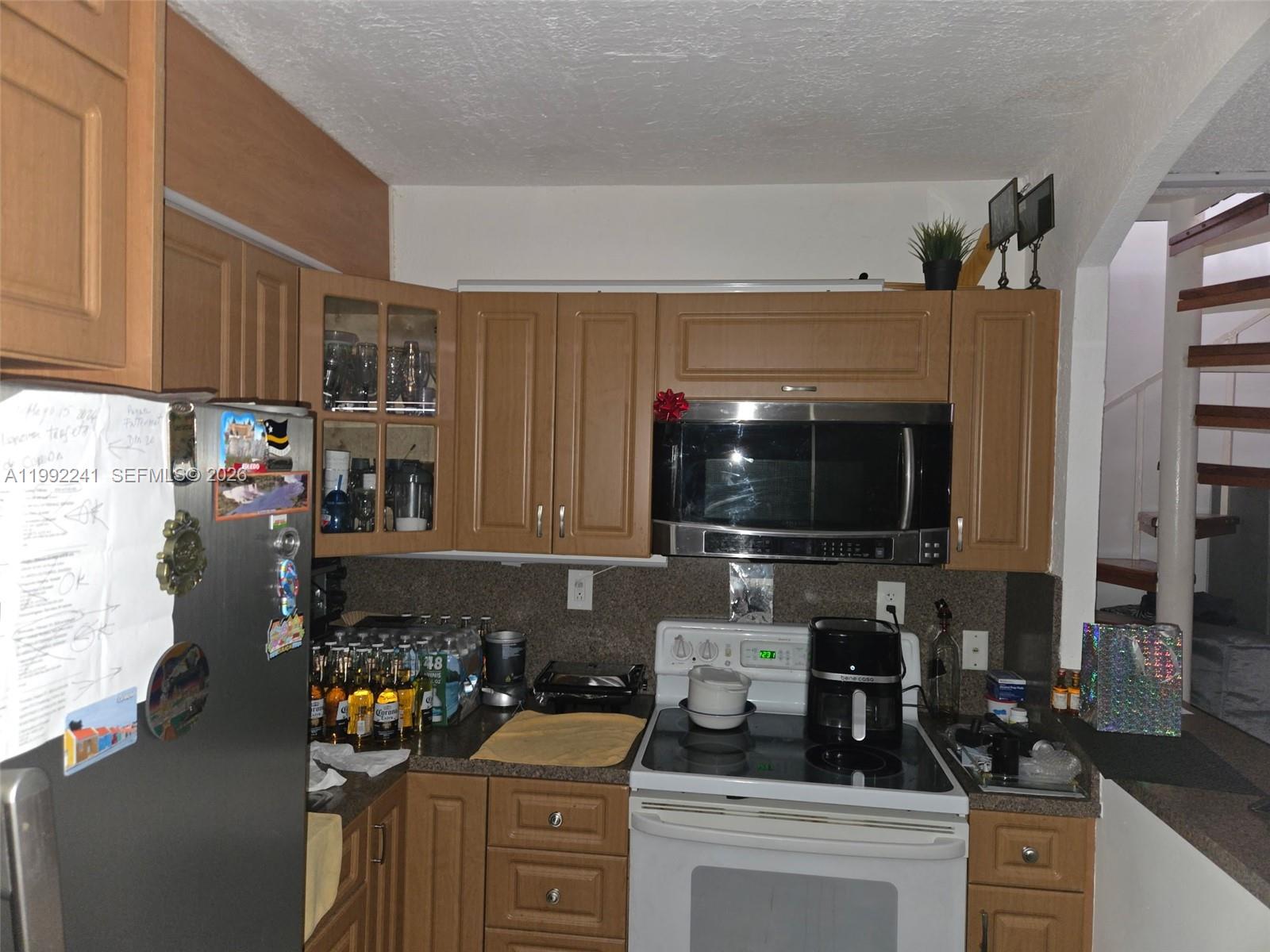 A kitchen features wood cabinets, a stainless steel microwave, a white stove, and a refrigerator — 6580 W Flagler St # 101, Miami FL 33144, MIAMI, FL