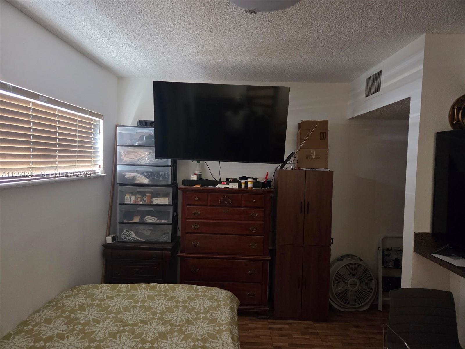 A bedroom features a bed, a dresser with a wall-mounted television, and storage units — 6580 W Flagler St # 101, Miami FL 33144, MIAMI, FL