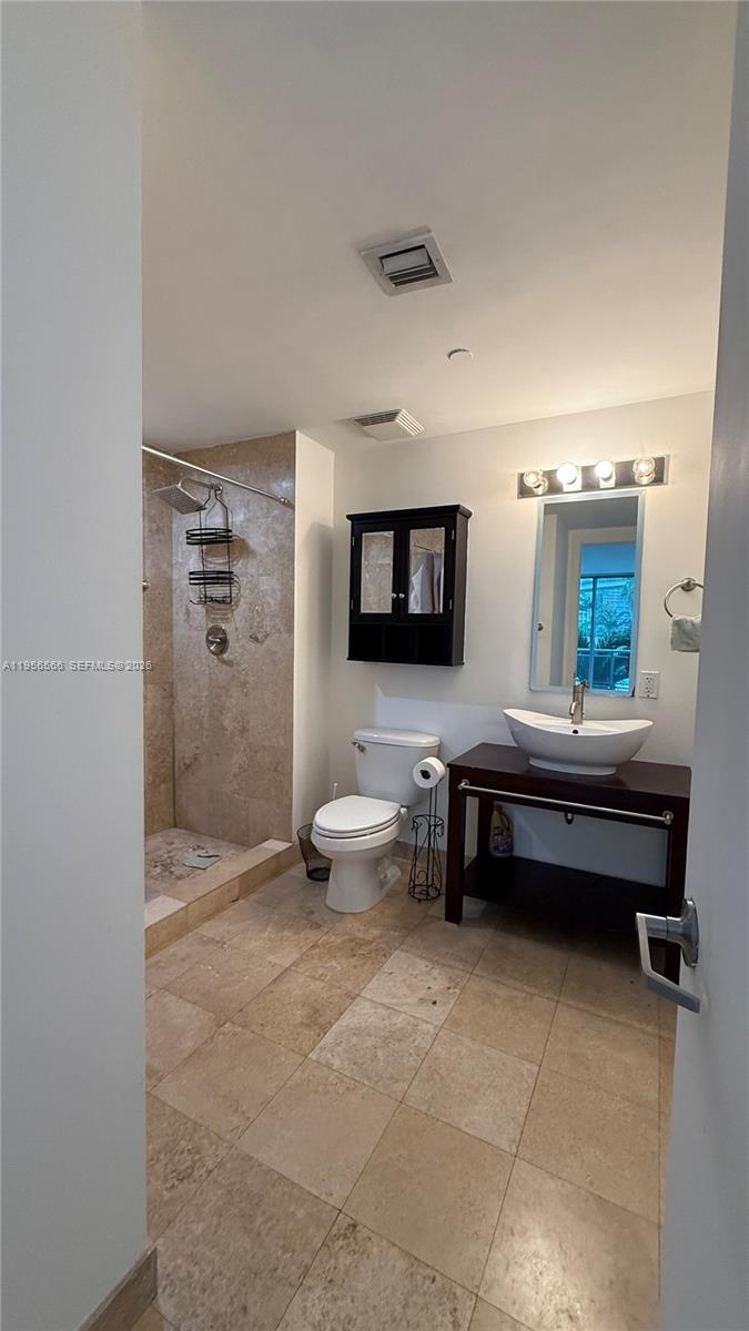 A bathroom features a walk-in shower with stone tile, a pedestal sink, and a toilet — 350 S Miami Ave # 304, Miami FL 33130, MIAMI, FL