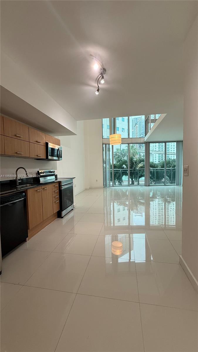 A modern kitchen with wood cabinets and stainless steel appliances opens to a bright living area — 350 S Miami Ave # 304, Miami FL 33130, MIAMI, FL