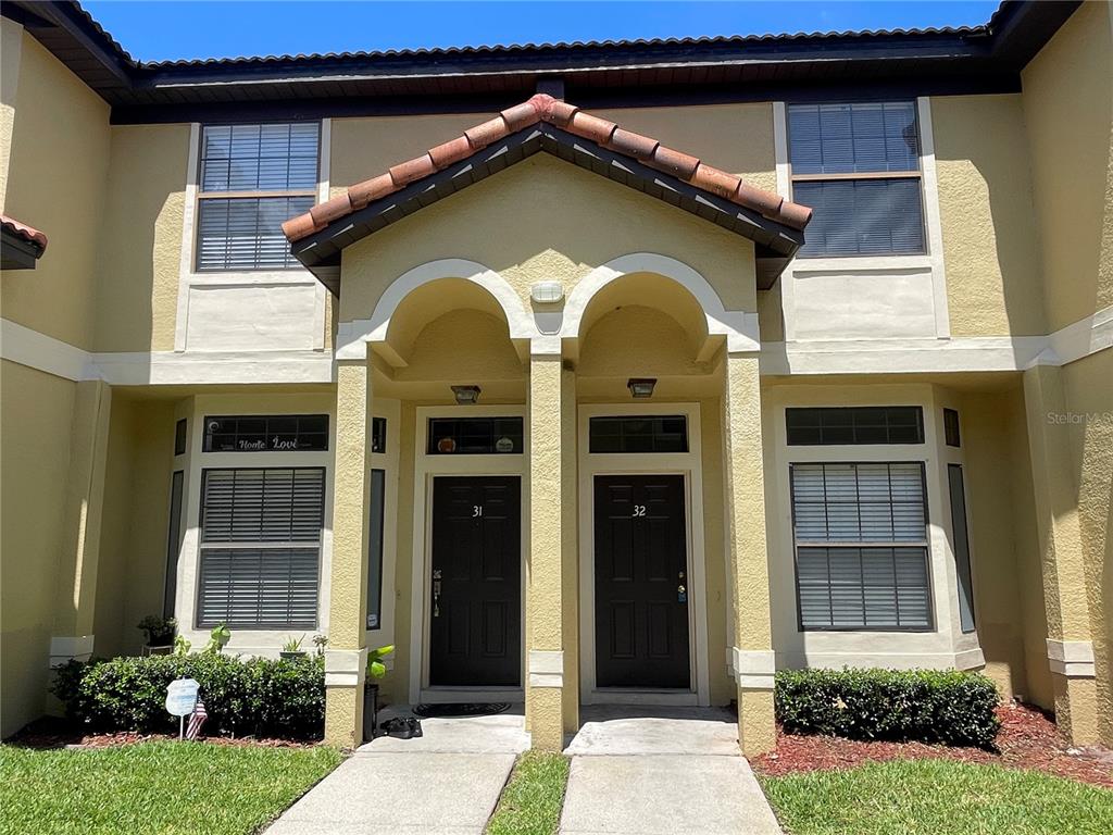 The exterior of a two-story tan stucco building features two adjacent front doors numbered 31 and 32 — 6007 SCOTCHWOOD GLEN UNIT 32, ORLANDO, FL