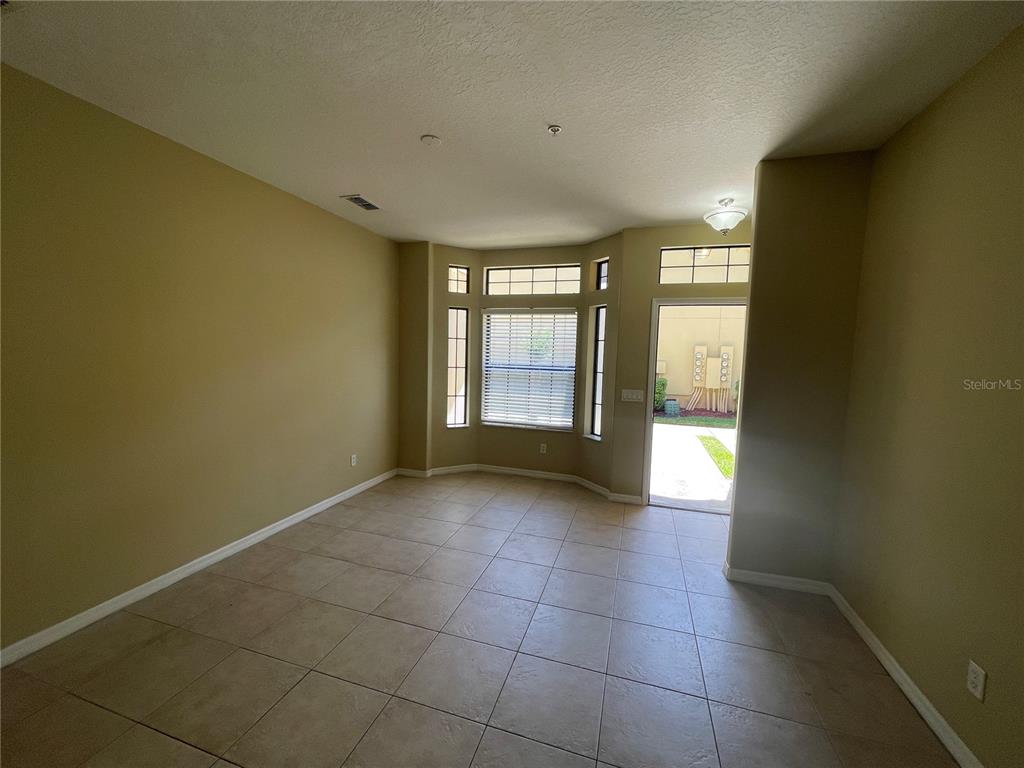 An empty room with beige walls, tile flooring, a bay window, and a glass door — 6007 SCOTCHWOOD GLEN UNIT 32, ORLANDO, FL