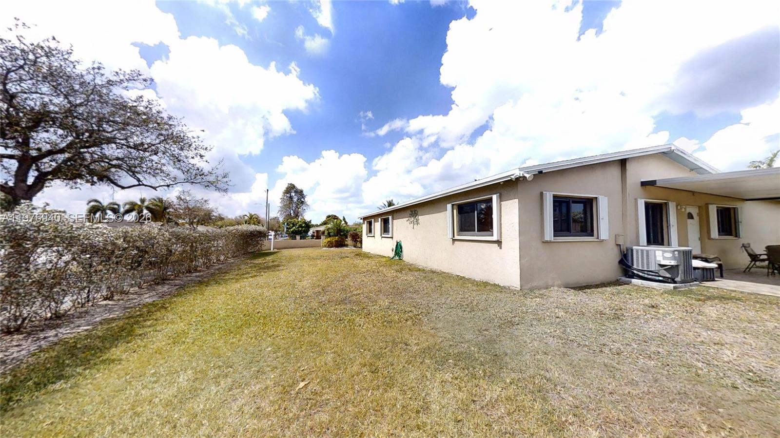 A beige house exterior features a grassy yard, a side patio, and an air conditioning unit — 705 NW 8th Ave, Florida City FL 33034, FLORIDA CITY, FL