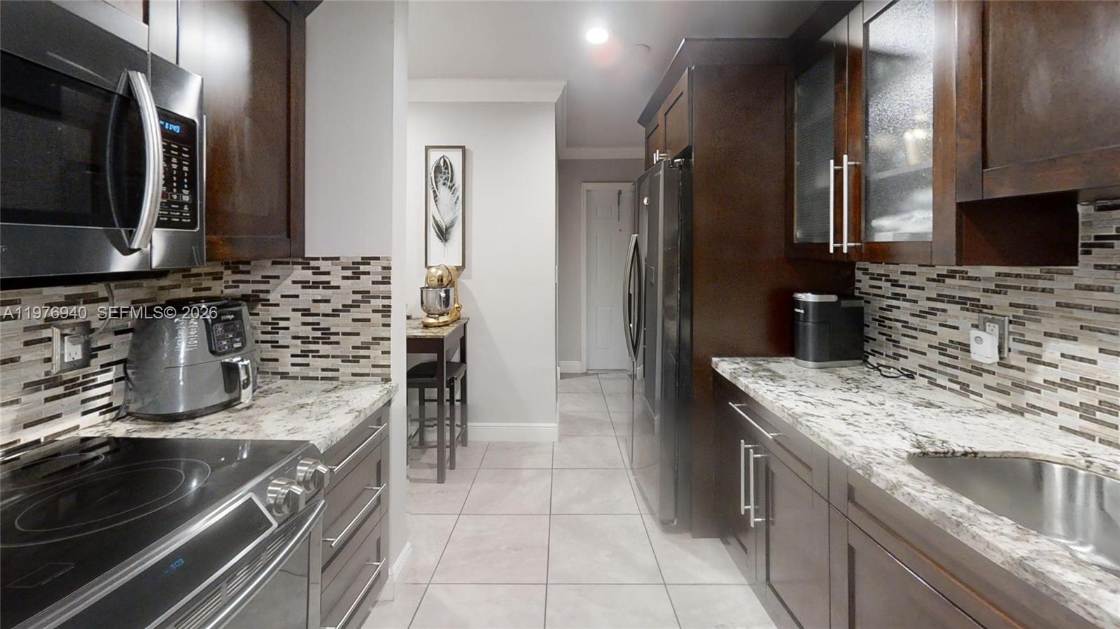 A galley kitchen features dark wood cabinets, granite countertops, and a tiled backsplash — 705 NW 8th Ave, Florida City FL 33034, FLORIDA CITY, FL
