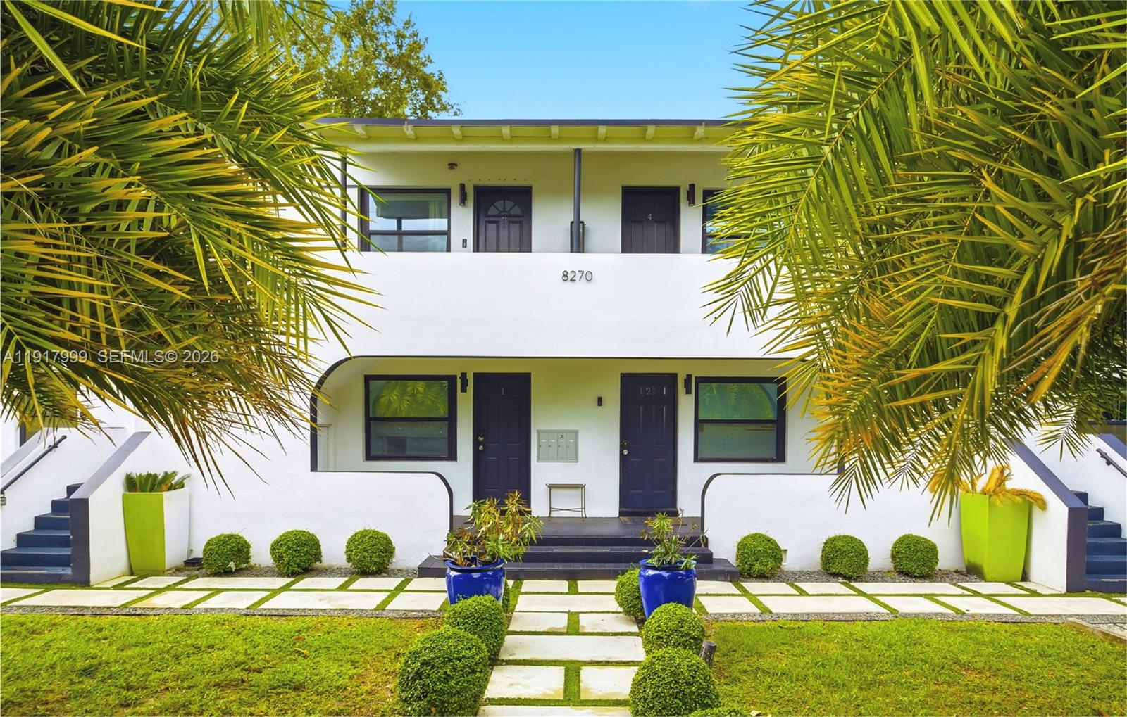 A two-story white apartment building features dark doors, palm trees, and a landscaped front yard — 8270 NE 1st Pl, Miami FL 33138, MIAMI, FL