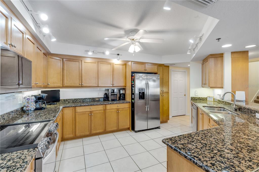 A kitchen with light wood cabinets, granite countertops, stainless steel appliances, and white tile flooring — 5300 S ATLANTIC AVENUE UNIT 8-601, NEW SMYRNA BEACH, FL