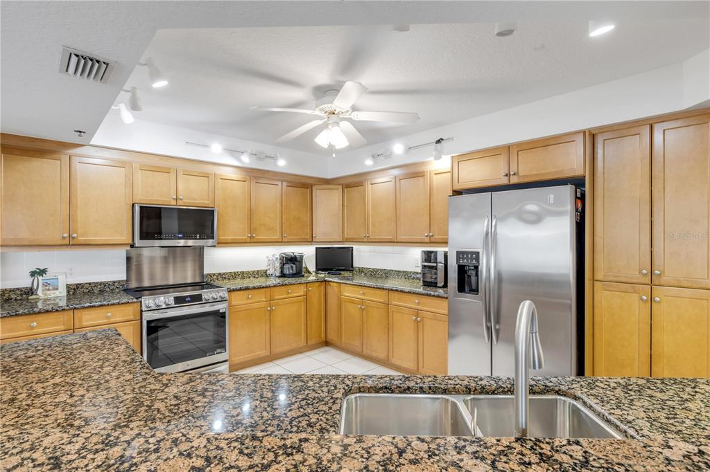 A kitchen features light wood cabinets, granite countertops, stainless steel appliances, and a ceiling fan — 5300 S ATLANTIC AVENUE UNIT 8-601, NEW SMYRNA BEACH, FL
