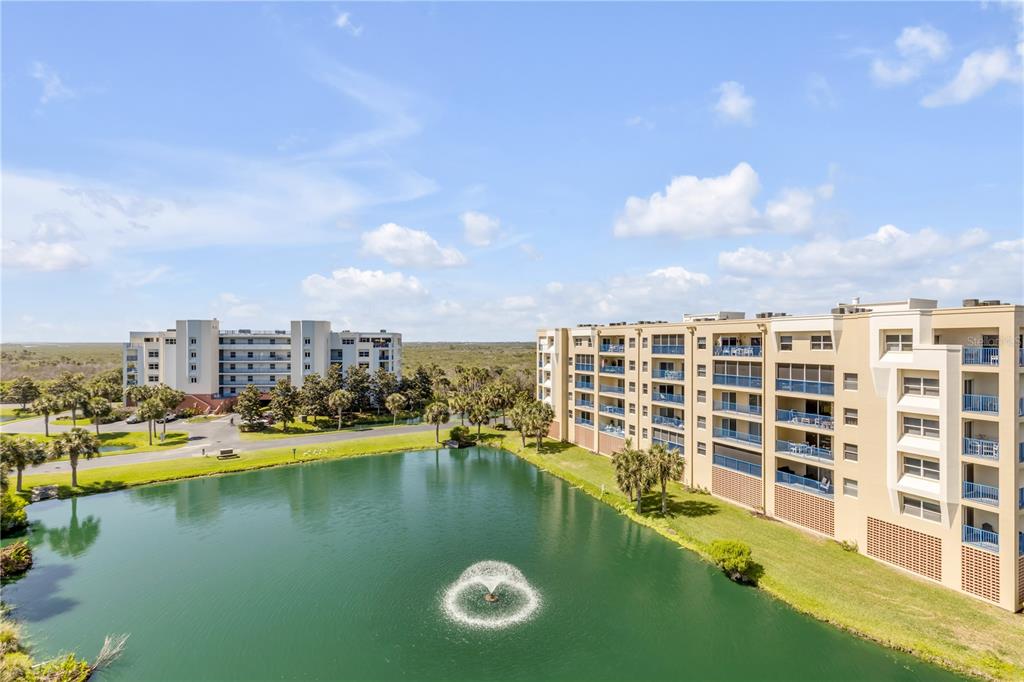 An exterior view of two multi-story apartment buildings overlooking a pond with a fountain — 5300 S ATLANTIC AVENUE UNIT 8-601, NEW SMYRNA BEACH, FL