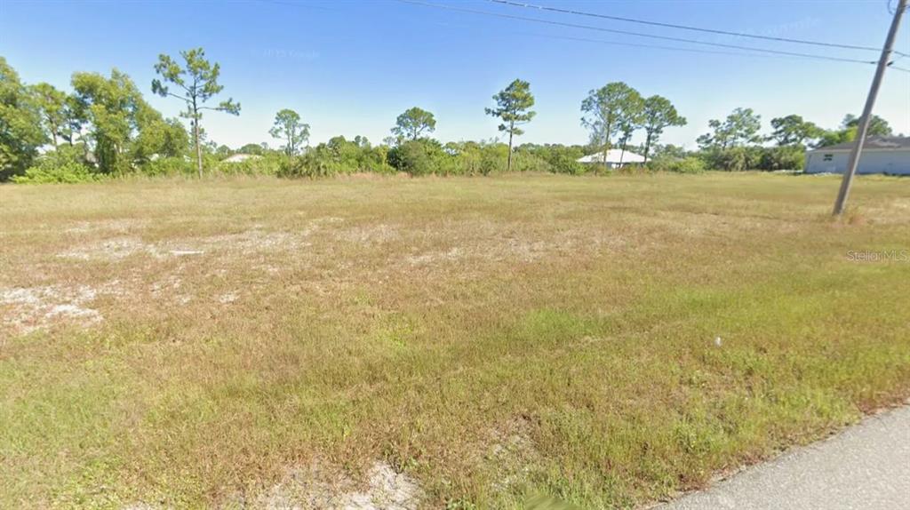 A flat, grassy vacant lot is bordered by trees under a clear blue sky — 1811 NE 44TH STREET, CAPE CORAL, FL