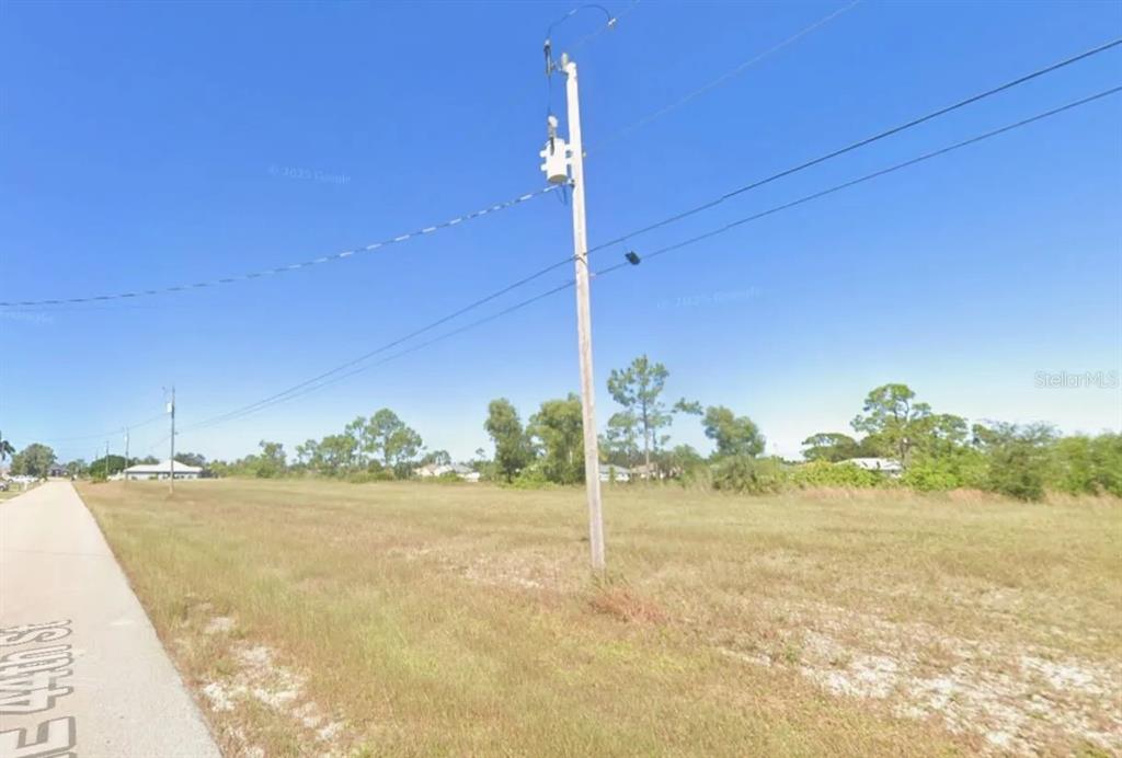 An empty, grassy lot sits beside a paved road with a utility pole in the foreground — 1811 NE 44TH STREET, CAPE CORAL, FL