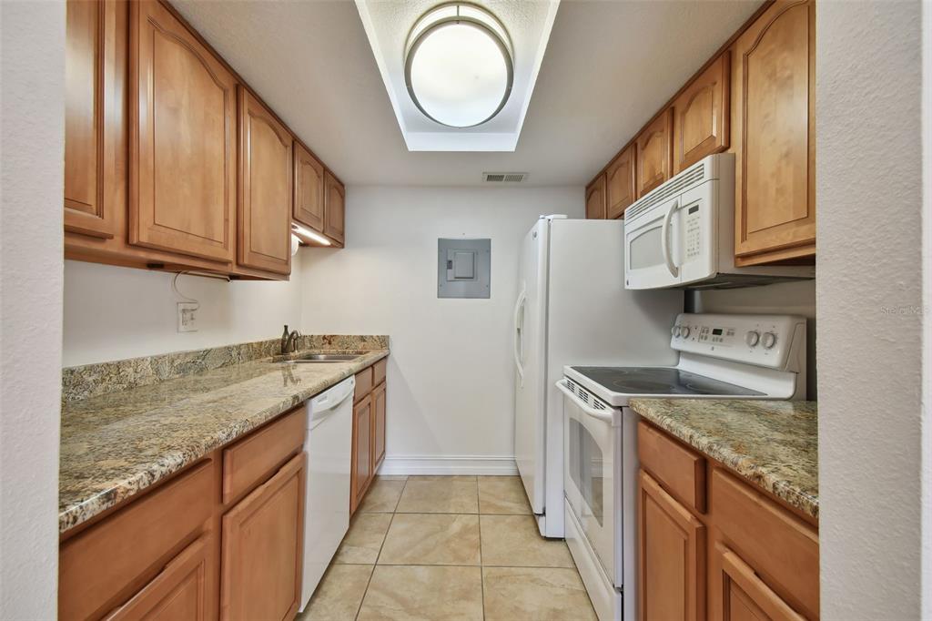 A galley-style kitchen features wood cabinets, granite countertops, white appliances, and a skylight — 8931 BLIND PASS ROAD UNIT 257, ST PETE BEACH, FL