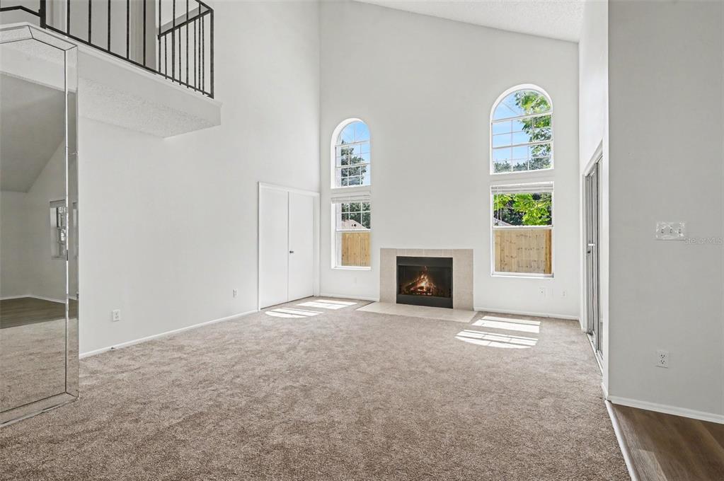 A living room with a vaulted ceiling, carpeted floor, fireplace, and arched windows — 311 TIBURON COURT, ORLANDO, FL