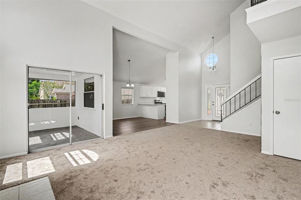 A living room with beige carpet, a sliding glass door, and stairs leading to a loft — 311 TIBURON COURT, ORLANDO, FL