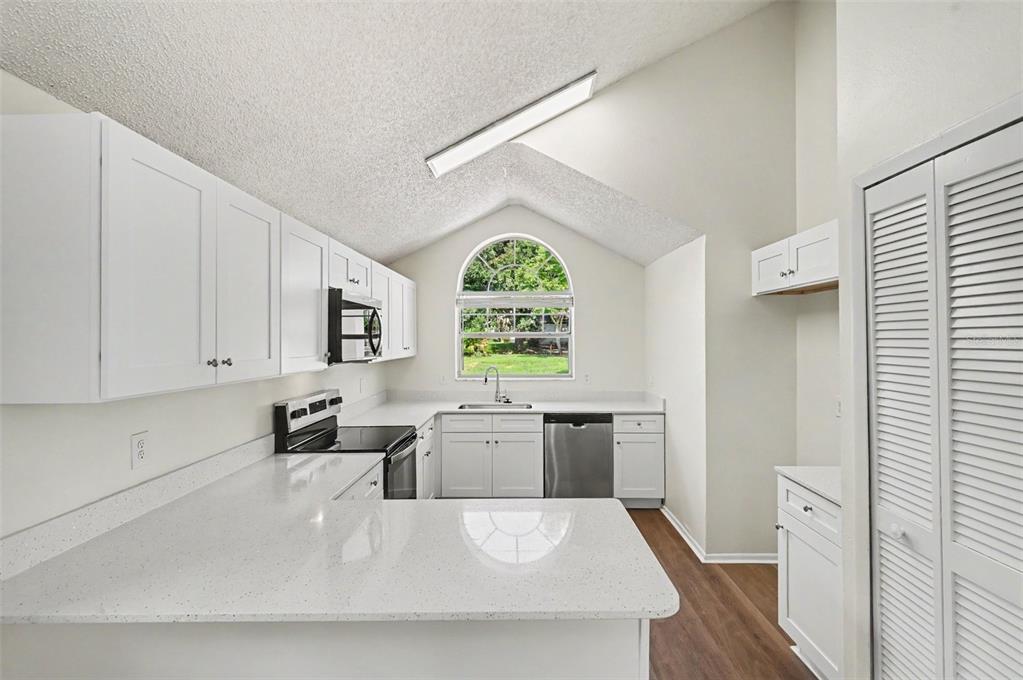 A kitchen with white cabinets, quartz countertops, stainless steel appliances, and an arched window — 311 TIBURON COURT, ORLANDO, FL