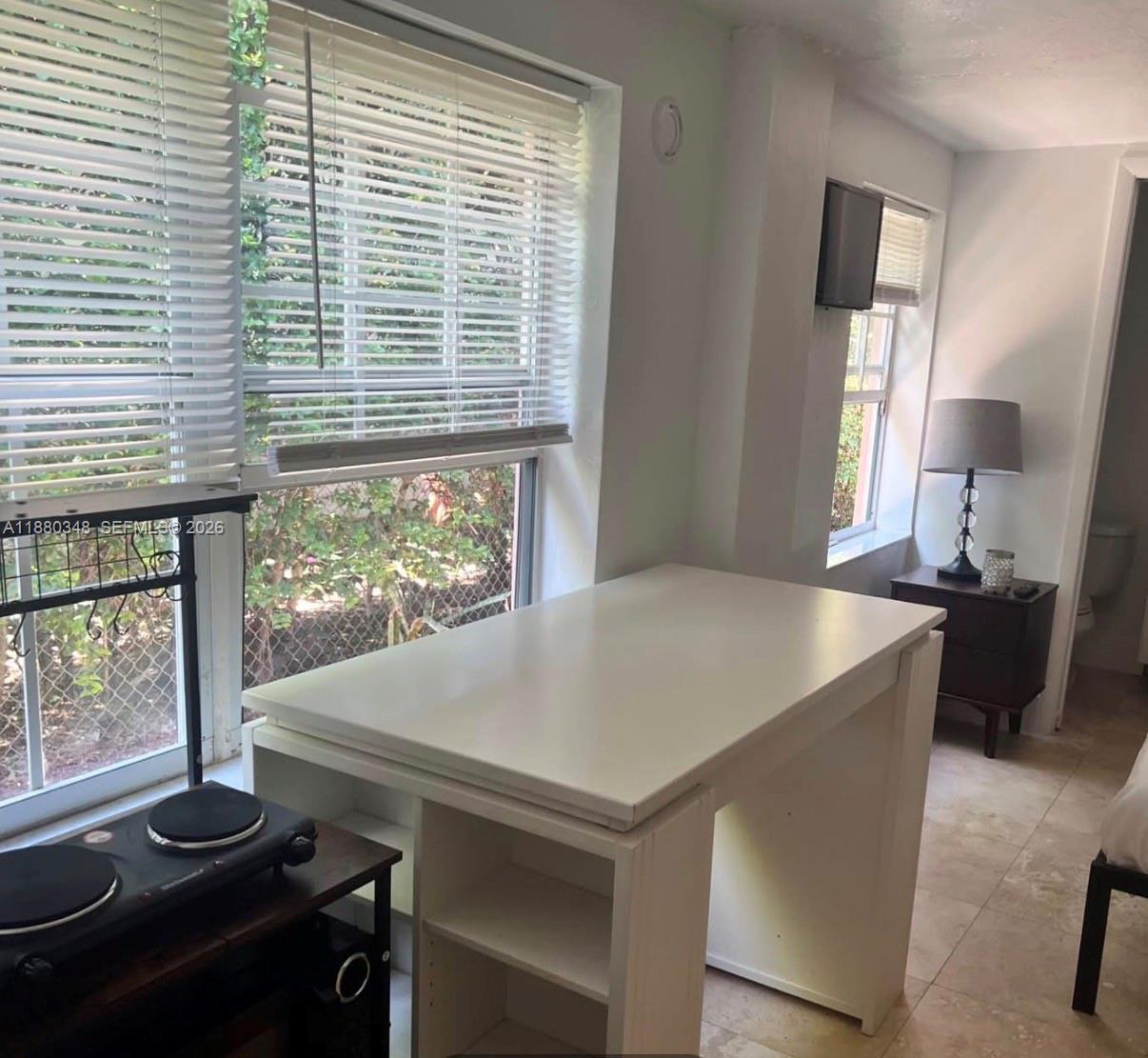 A room features a white table, a window with blinds, and a small side table — 1949 NE 173rd St # 0, North Miami Beach FL 33162, NORTH MIAMI BEACH, FL