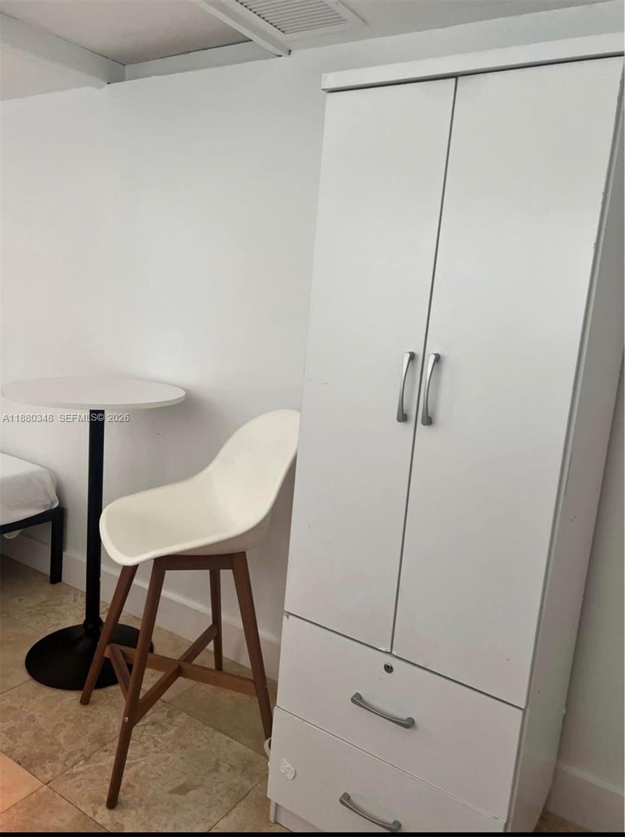 A white wardrobe stands next to a small round table and a modern chair — 1949 NE 173rd St # 0, North Miami Beach FL 33162, NORTH MIAMI BEACH, FL