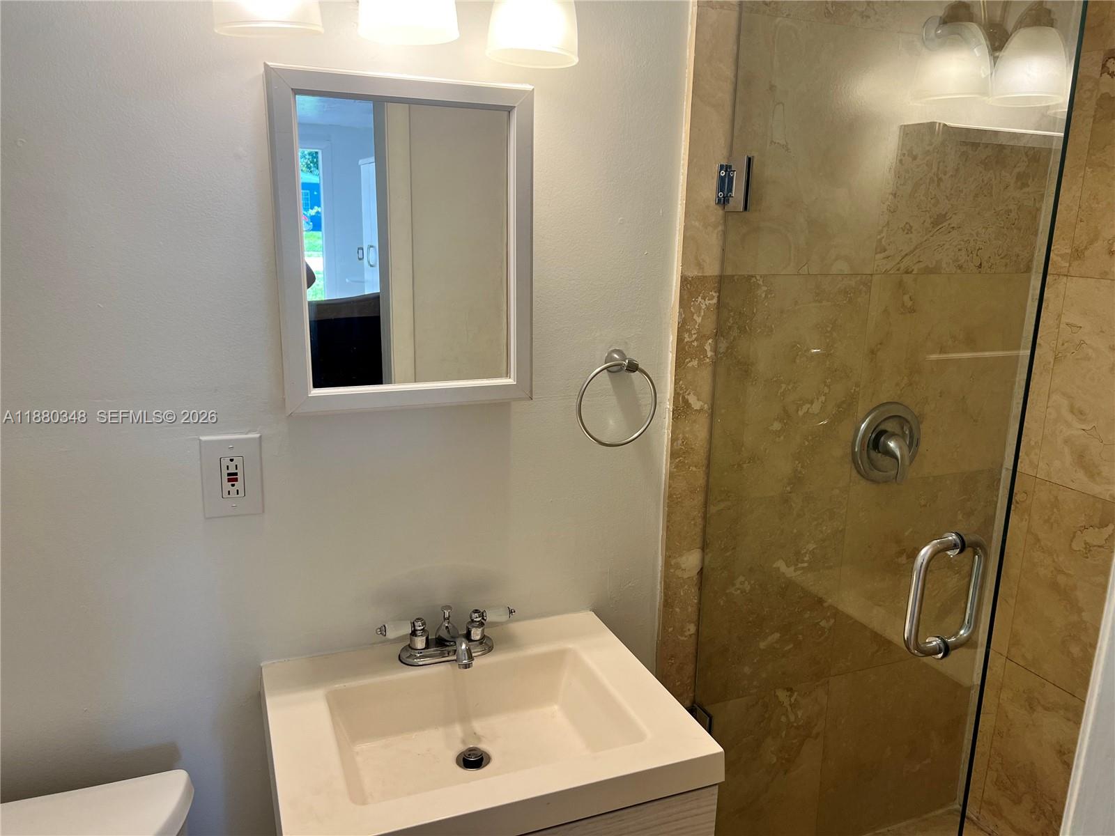 A bathroom features a white vanity, a wall-mounted mirror, and a glass-enclosed tiled shower — 1949 NE 173rd St # 0, North Miami Beach FL 33162, NORTH MIAMI BEACH, FL