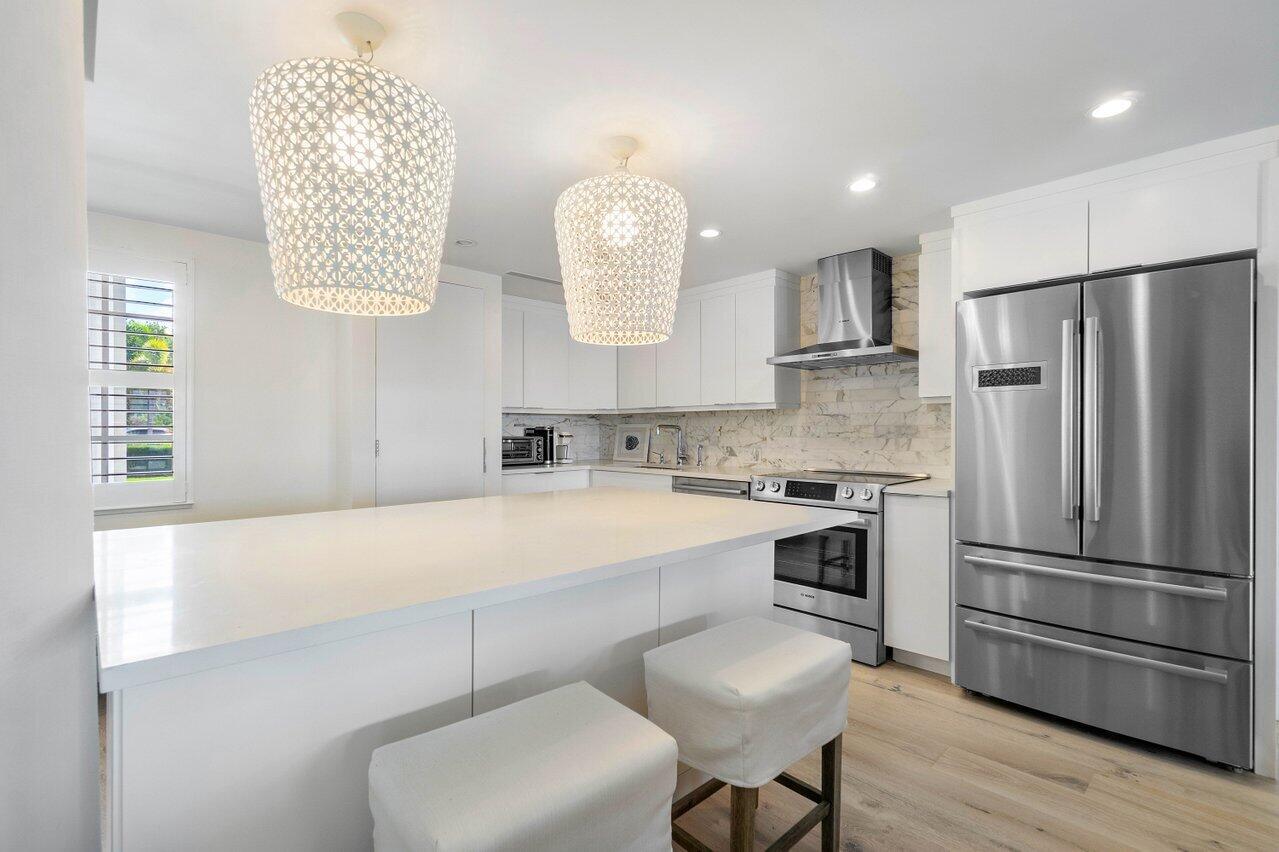 A modern kitchen features white cabinetry, a large island with stools, and stainless steel appliances — 2170 Ibis Isle Road # 3, Palm Beach FL 33480, PALM BEACH, FL