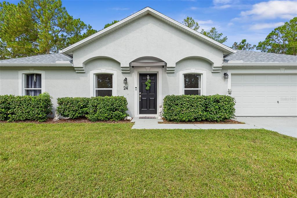 A single-story house with a light gray exterior, a black front door, and manicured hedges — 24 SEDGWICK TRAIL, PALM COAST, FL