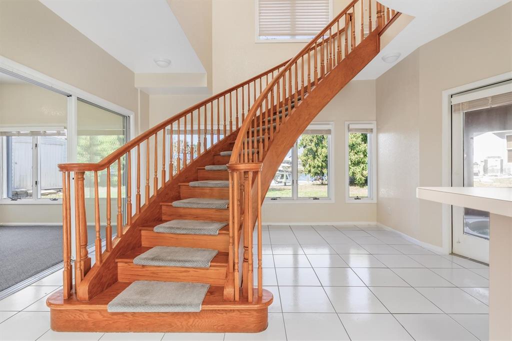 A curved wooden staircase with carpet treads stands in a room with white tile floors — 4405 HARBOR BOULEVARD, PORT CHARLOTTE, FL