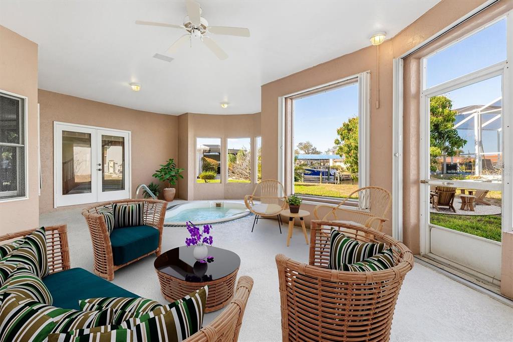 A sunroom features a built-in hot tub, wicker furniture, and large windows overlooking a canal — 4405 HARBOR BOULEVARD, PORT CHARLOTTE, FL