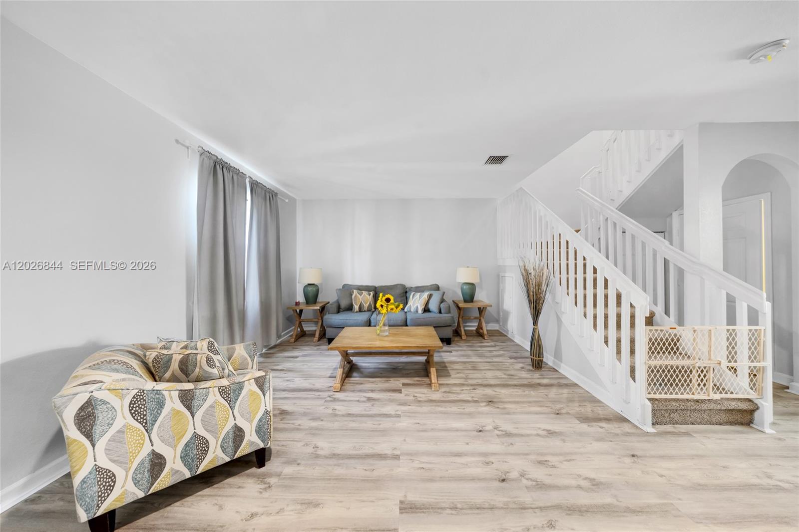 A living room features light wood-look flooring, a grey sofa, and a white staircase — 9381 W 33rd Ln, Hialeah FL 33018, HIALEAH, FL