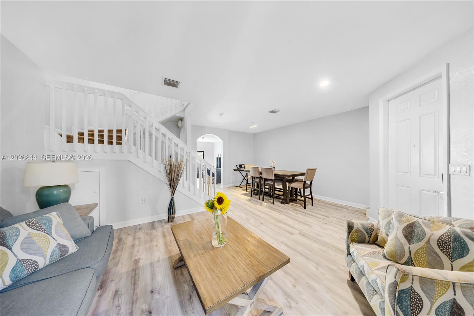 A living room and dining area with light wood flooring and a white staircase — 9381 W 33rd Ln, Hialeah FL 33018, HIALEAH, FL