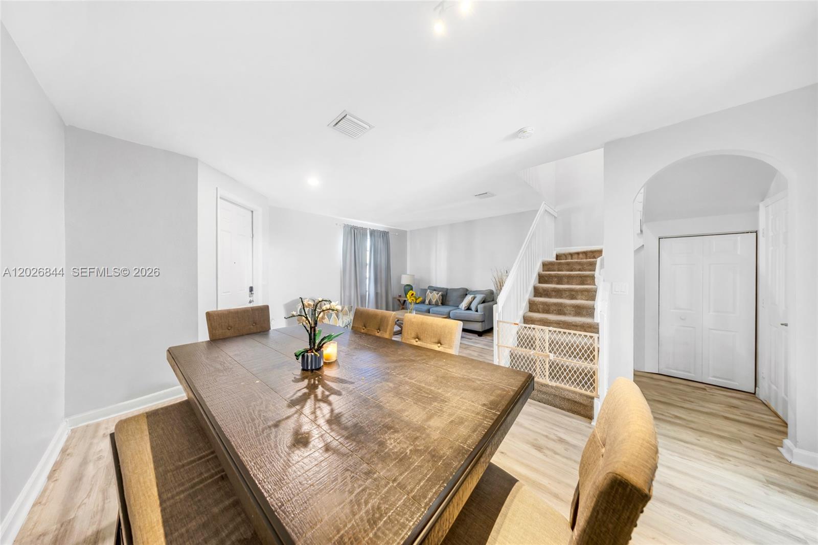 A dining area with a wooden table sits in front of a living room and staircase — 9381 W 33rd Ln, Hialeah FL 33018, HIALEAH, FL