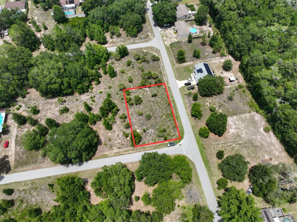 An aerial view shows a vacant, rectangular lot outlined in red situated between two roads — SW 82ND PL, DUNNELLON, FL
