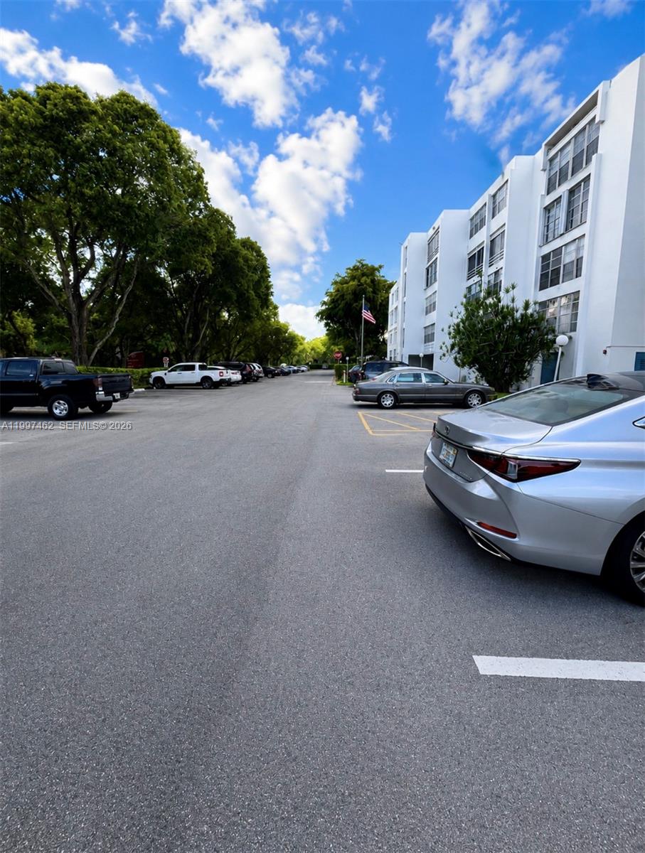An outdoor parking lot sits beside a multi-story white apartment building under a blue sky — 6901 Cypress Rd # B17, Plantation FL 33317, PLANTATION, FL