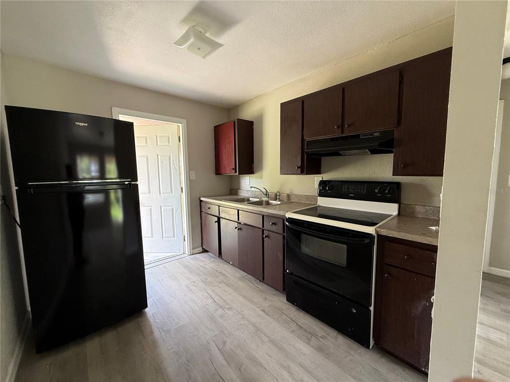 A kitchen features dark wood cabinets, black appliances, and light wood-look flooring — 116 COURT STREET SW, FORT MEADE, FL