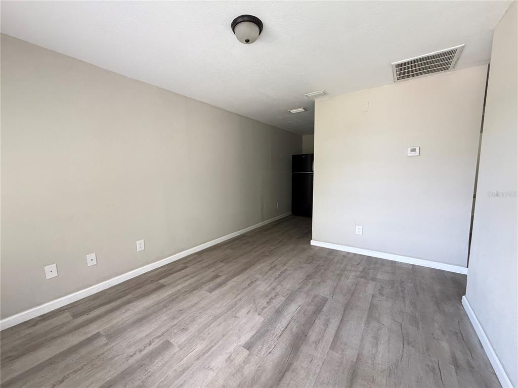 An empty room with light-colored walls, wood-look flooring, and a view of a kitchen area — 116 COURT STREET SW, FORT MEADE, FL