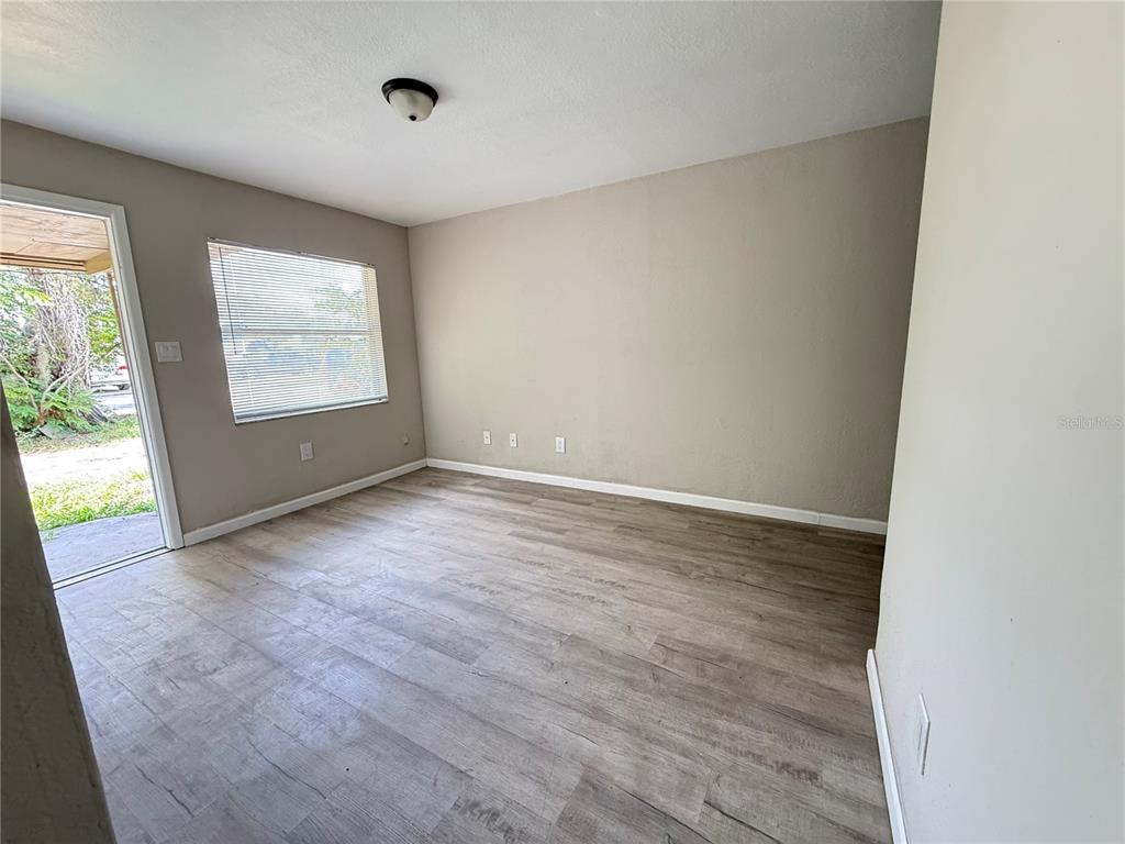 An empty room features light-colored walls, wood-look flooring, a window with blinds, and an exterior door — 116 COURT STREET SW, FORT MEADE, FL