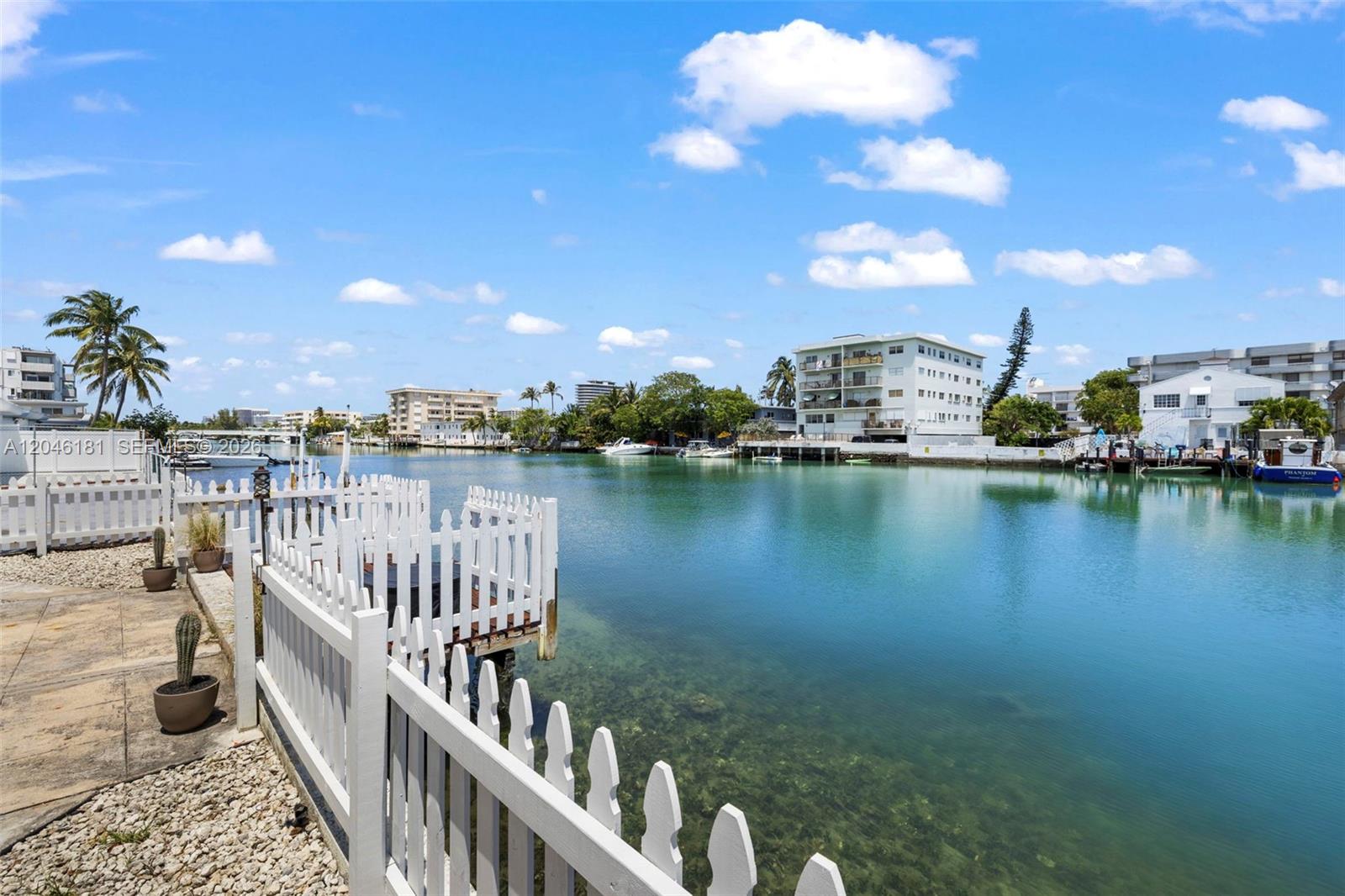 A white picket fence borders a canal with boats and residential buildings in the background — 8135 Crespi Blvd # 4, Miami Beach FL 33141, MIAMI BEACH, FL