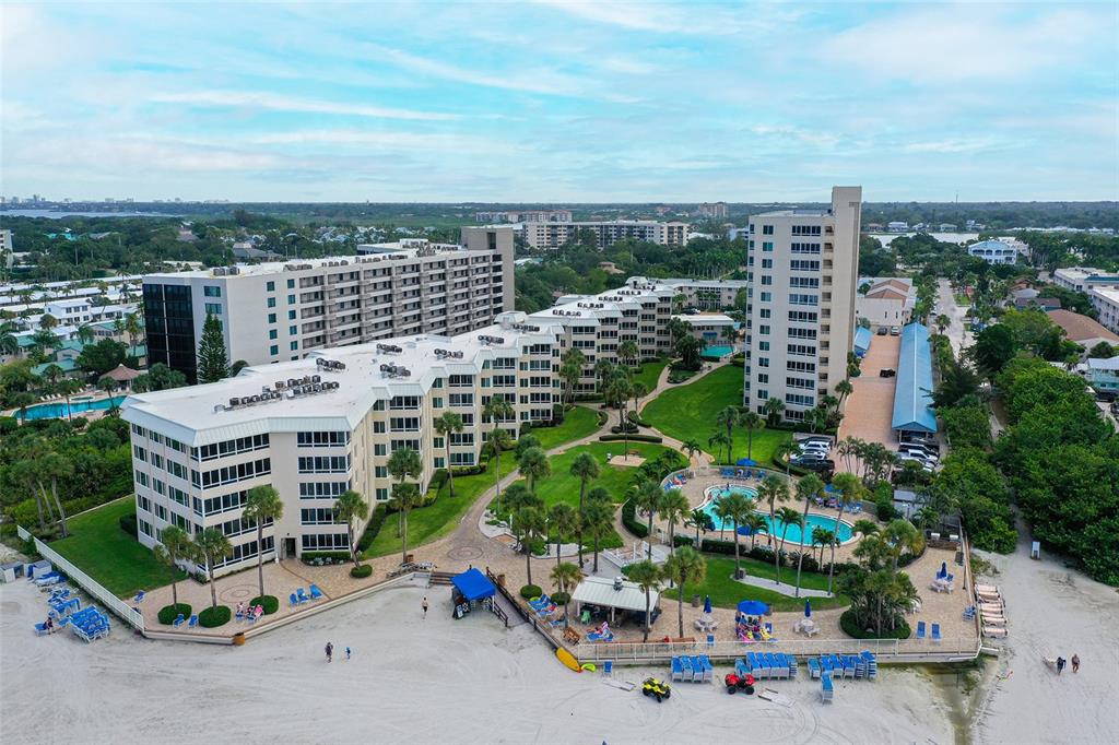 An aerial view shows a multi-story beachfront condominium complex with pools and palm trees — 5920 MIDNIGHT PASS ROAD UNIT 406, SARASOTA, FL