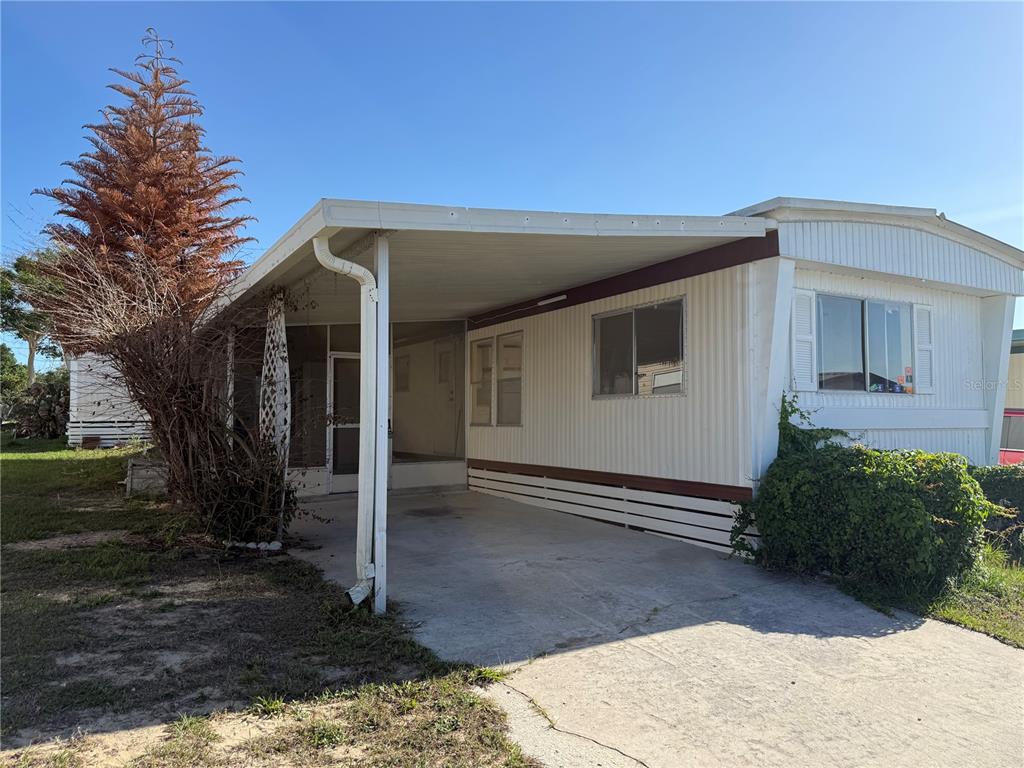 A single-story mobile home features a concrete driveway, a carport, and a screened-in porch area — 17730 US HWY 27 UNIT 43, CLERMONT, FL