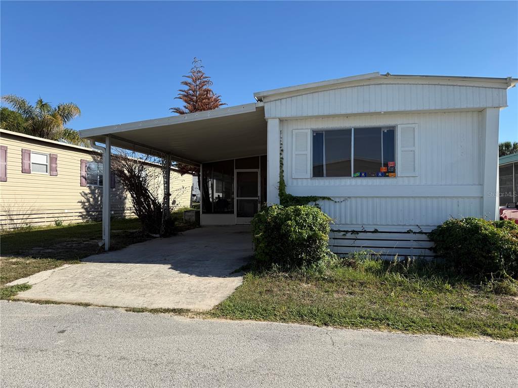 A white mobile home features a concrete carport and a screened-in porch entrance — 17730 US HWY 27 UNIT 43, CLERMONT, FL