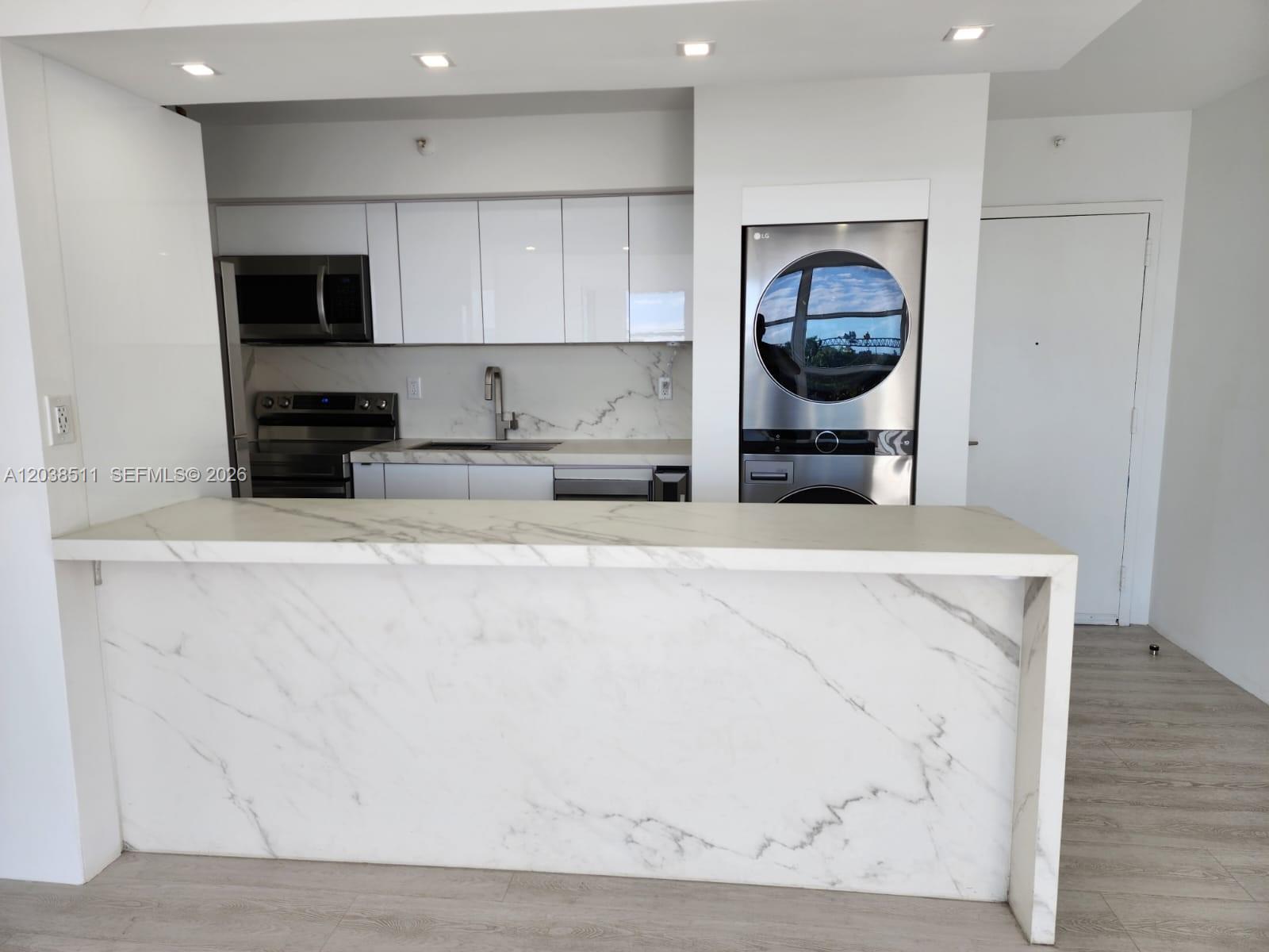 A modern kitchen features white cabinetry, marble countertops, and a stacked washer-dryer unit — 1700 NW N River Dr # 606, Miami FL 33125, MIAMI, FL