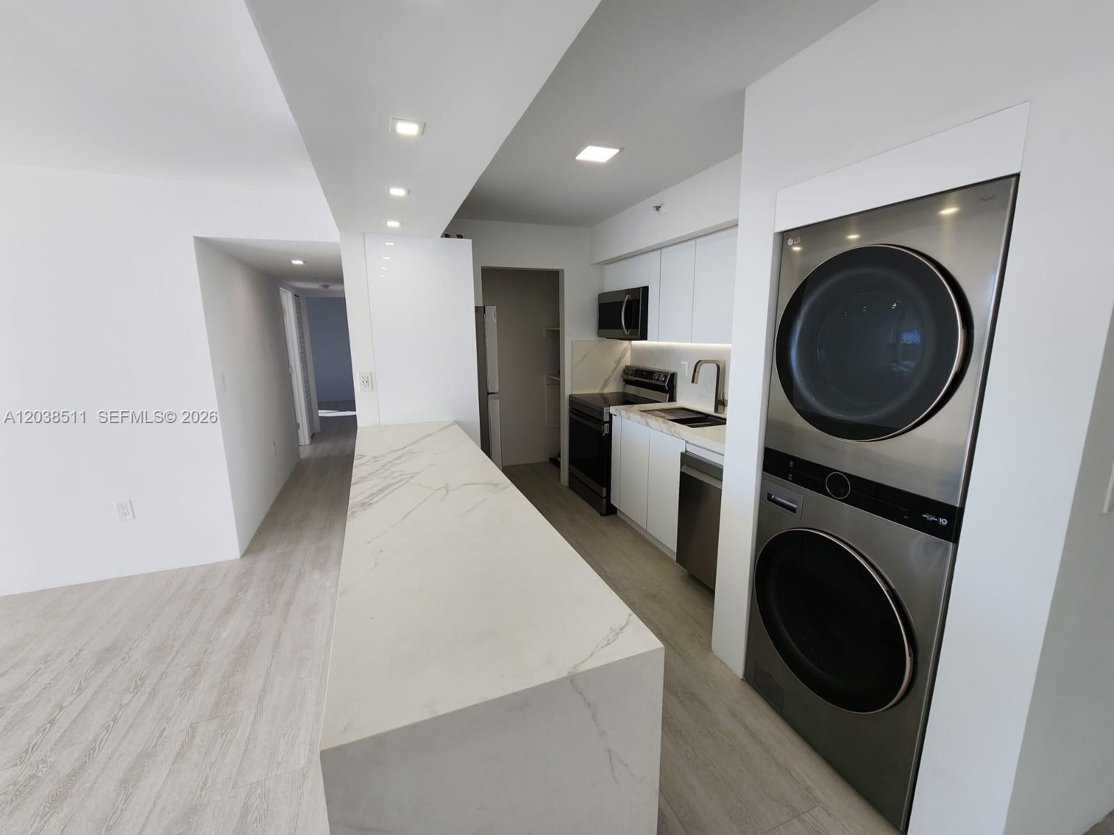 A modern kitchen features a marble-topped island, white cabinetry, and a stacked stainless steel washer-dryer — 1700 NW N River Dr # 606, Miami FL 33125, MIAMI, FL