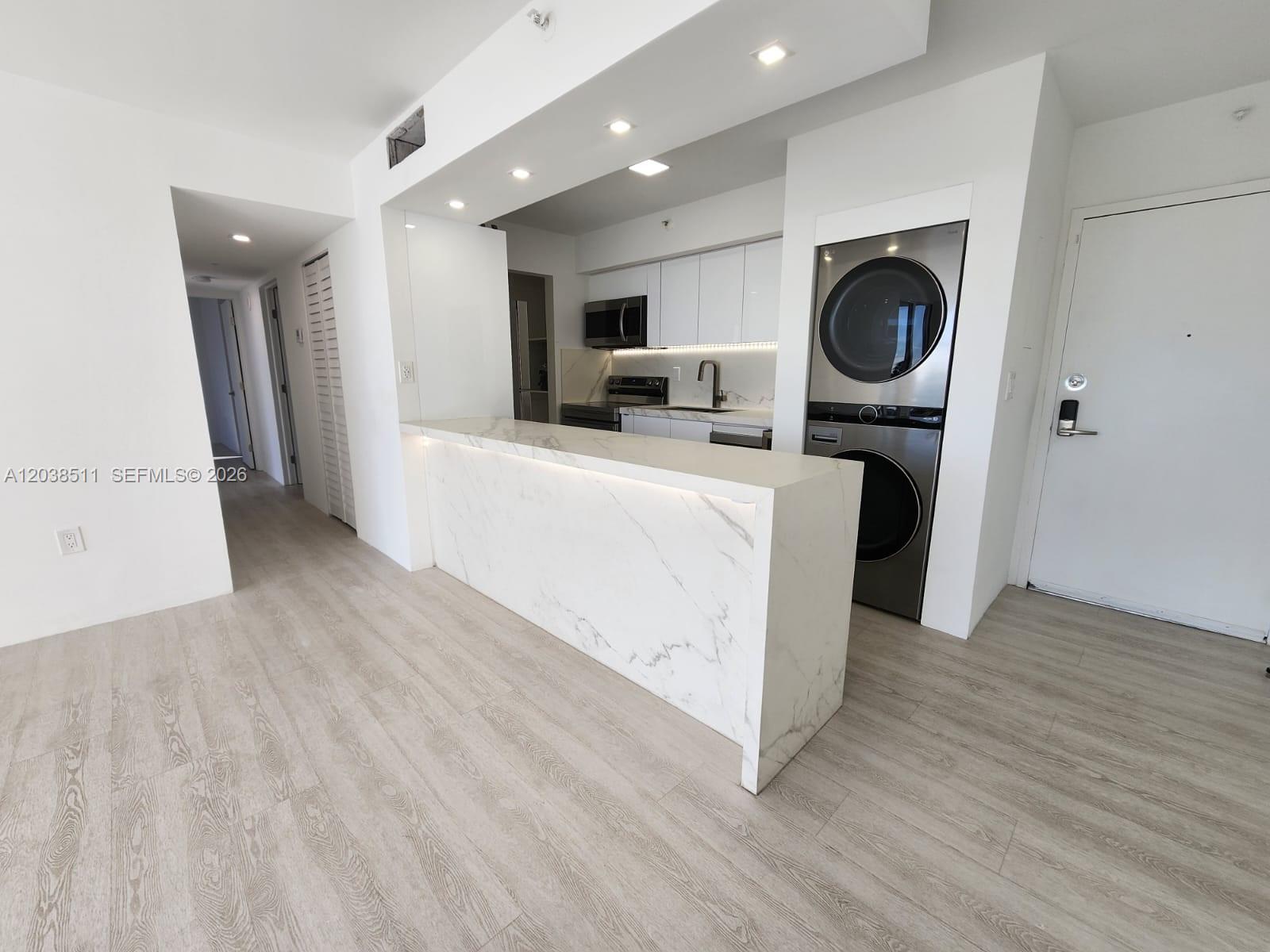 A modern kitchen features a marble waterfall island, white cabinetry, and a stacked laundry unit — 1700 NW N River Dr # 606, Miami FL 33125, MIAMI, FL