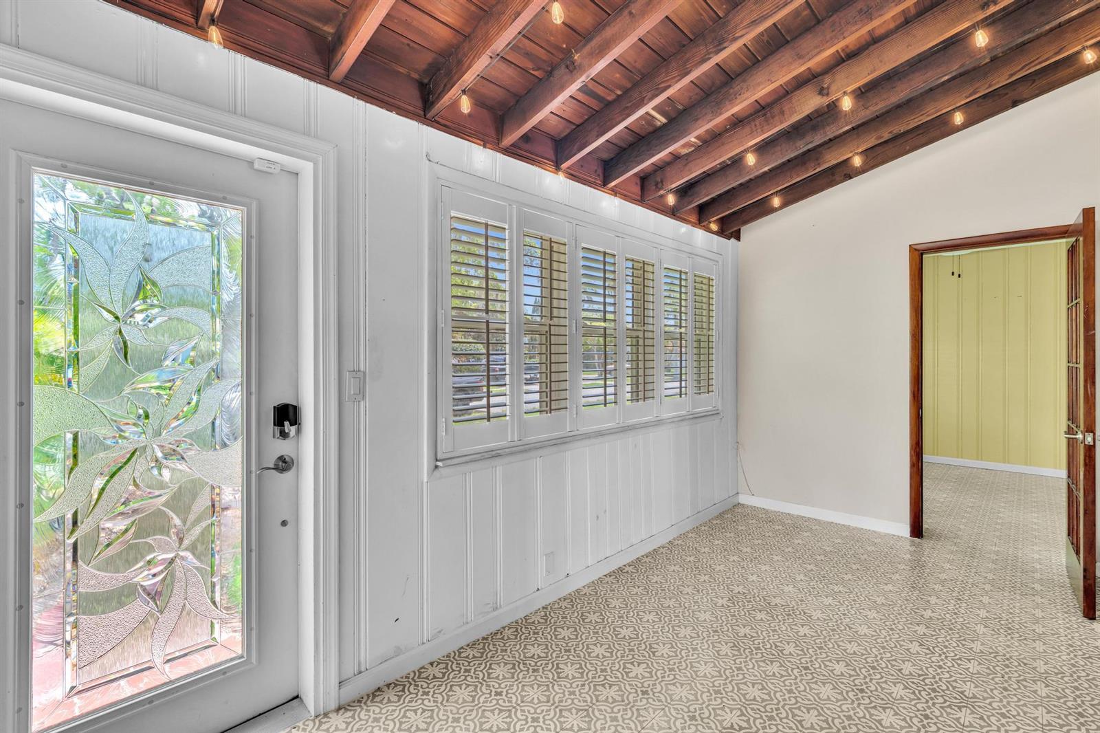 A sunroom with a patterned tile floor, white paneled walls, and an exposed wood ceiling — 1527 Mayo Street, Hollywood FL 33020, HOLLYWOOD, FL