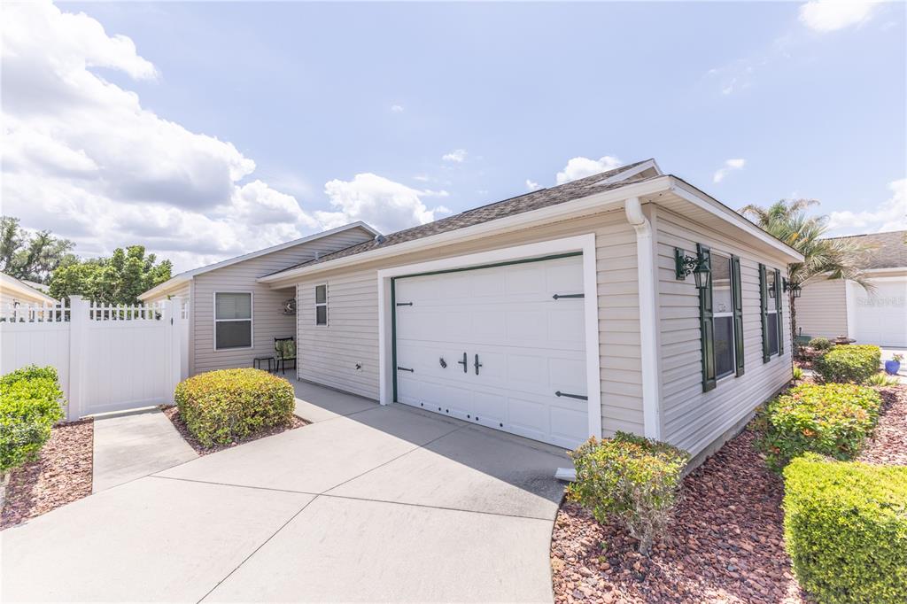 A beige house exterior features a white garage door, a concrete driveway, and white fencing — 2306 NACKMAN PLACE, THE VILLAGES, FL