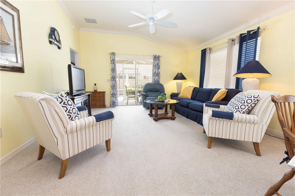 A living room with yellow walls, a blue sofa, two striped armchairs, and a ceiling fan — 2306 NACKMAN PLACE, THE VILLAGES, FL
