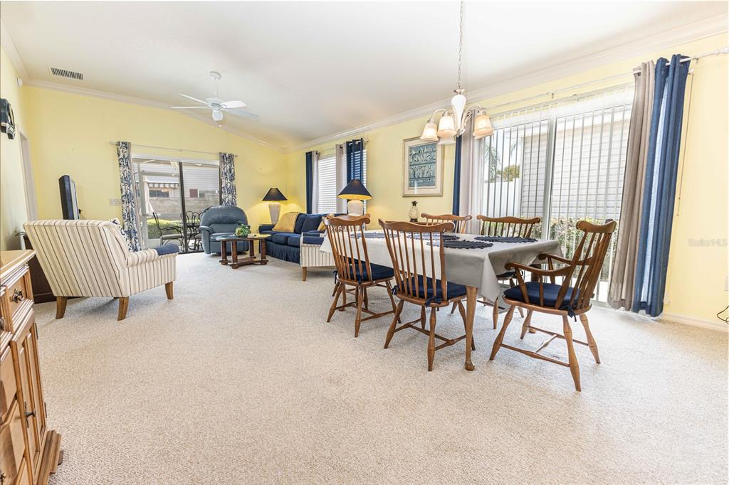 A living and dining room with yellow walls, carpeted floors, and sliding glass patio doors — 2306 NACKMAN PLACE, THE VILLAGES, FL