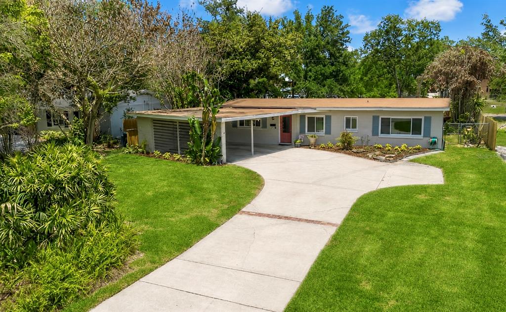 A single-story house with a carport, concrete driveway, and front lawn under a blue sky — 2215 WOODCREST DRIVE, WINTER PARK, FL