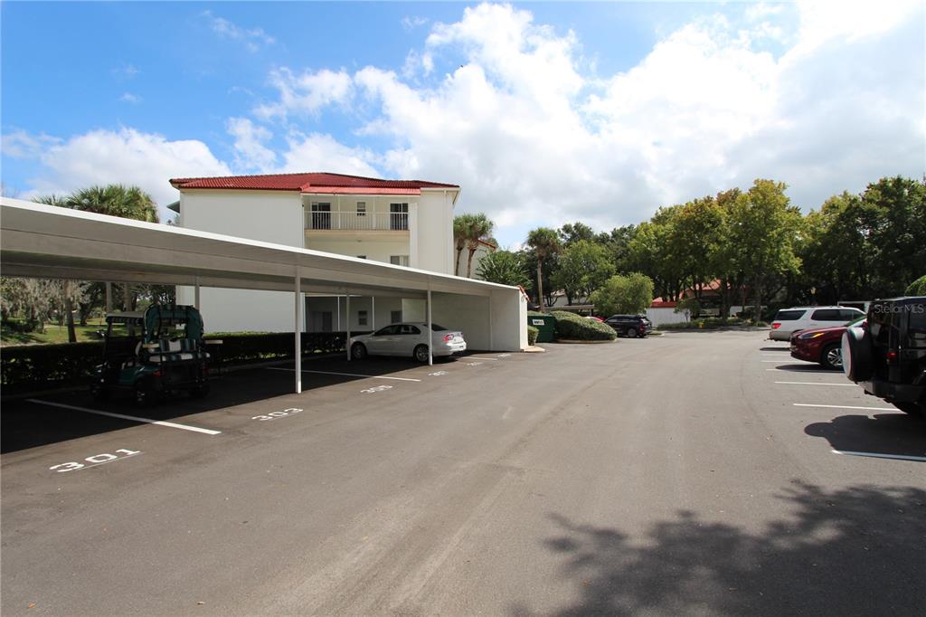 A covered parking area with numbered spaces sits in front of a multi-story apartment building — 451 HAMPTONCREST CIRCLE UNIT 307, LAKE MARY, FL