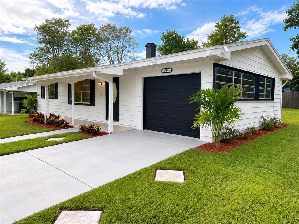 A white single-story house features a black garage door, a covered porch, and landscaped lawn — 14565 SW 35TH TERRACE ROAD, OCALA, FL