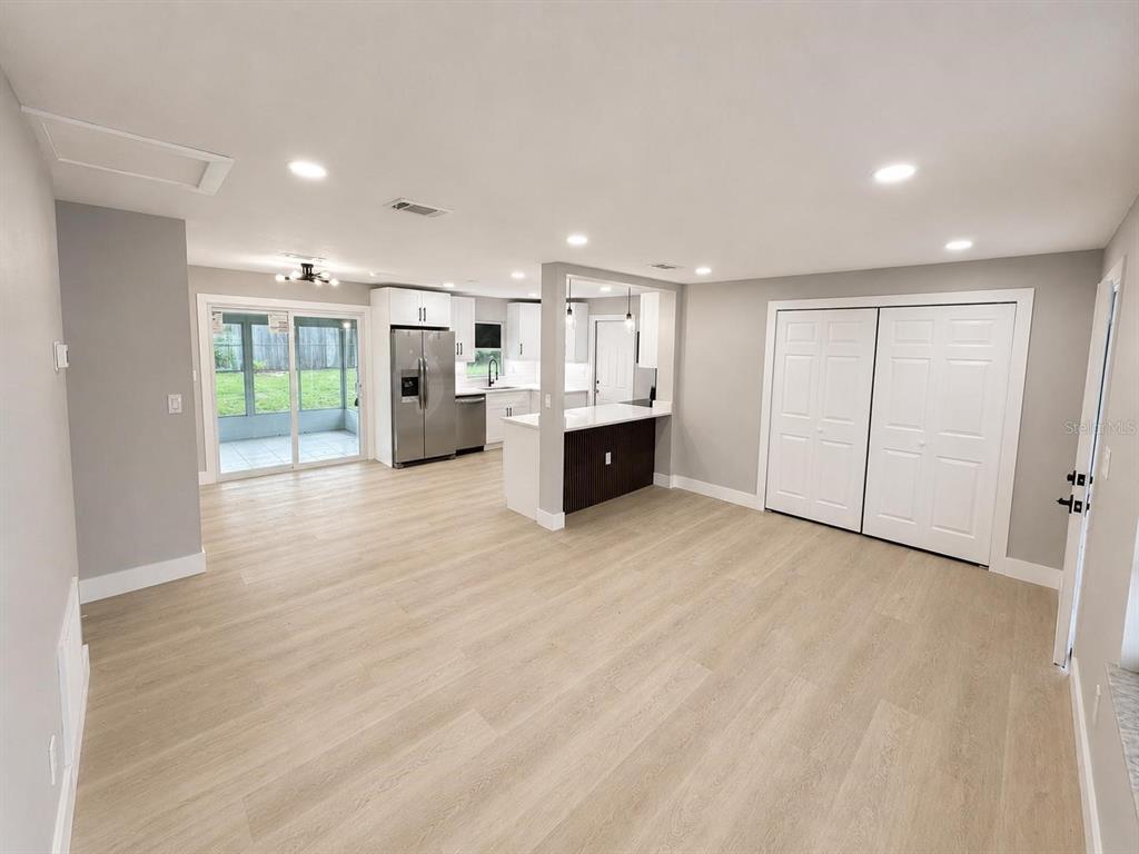 A bright, open-concept living area features light wood-look flooring, a modern kitchen, and sliding doors — 14565 SW 35TH TERRACE ROAD, OCALA, FL