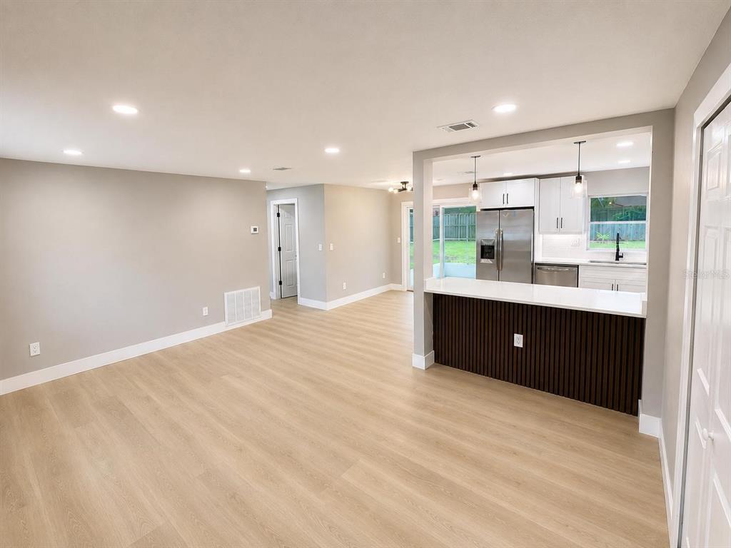 A living room with light wood flooring flows into a kitchen featuring a slatted breakfast bar — 14565 SW 35TH TERRACE ROAD, OCALA, FL